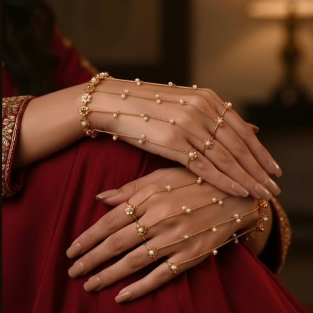 This elegant piece features fine gold-tone chains adorned with dainty faux pearls and floral accents, forming a delicate web that drapes beautifully across the back of the hand and fingers. The minimalist yet regal design makes it ideal for brides, bridesmaids, and anyone who loves soft, feminine jewellery.