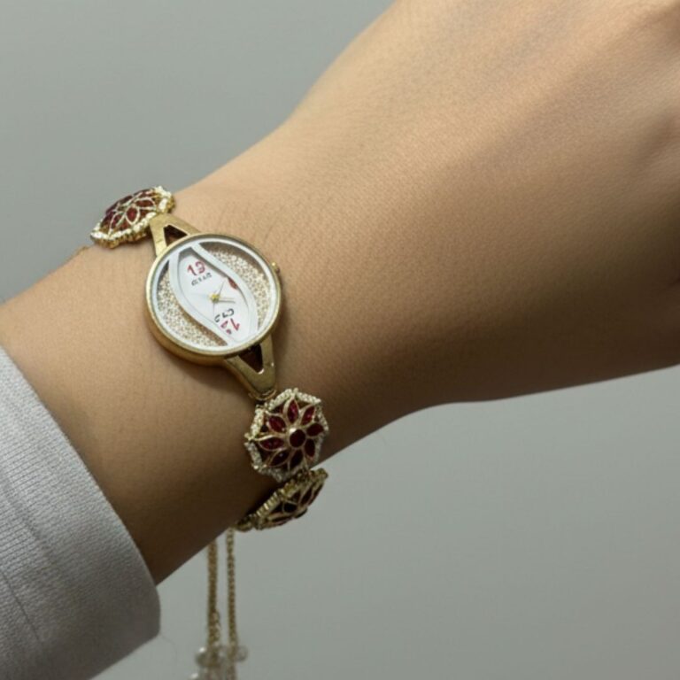 Gold floral watch bracelet with ruby stones, pearl detailing and chain tassels on wooden tray.