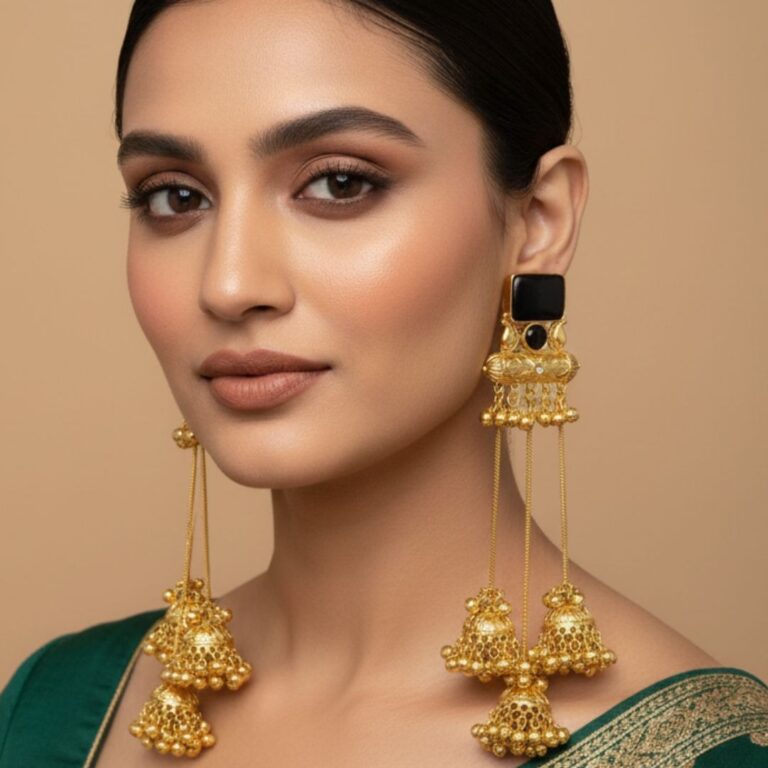 Gold long jhumka earrings with chain drops and multiple ghungroo clusters in pink and black stone variants held in hand.